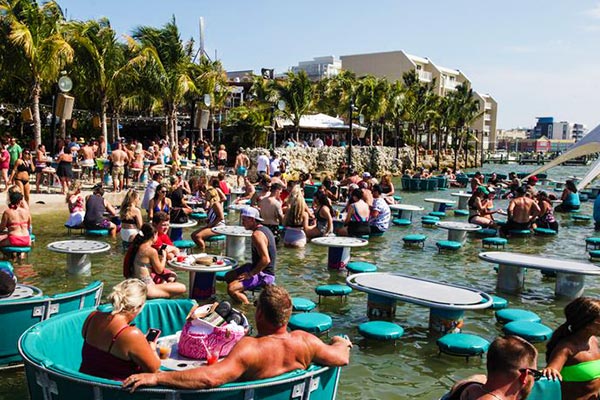 A crowded beach with tables and chairs in the water and guests enjoying