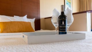 A bottle of wine and two glasses on a neatly folded bed