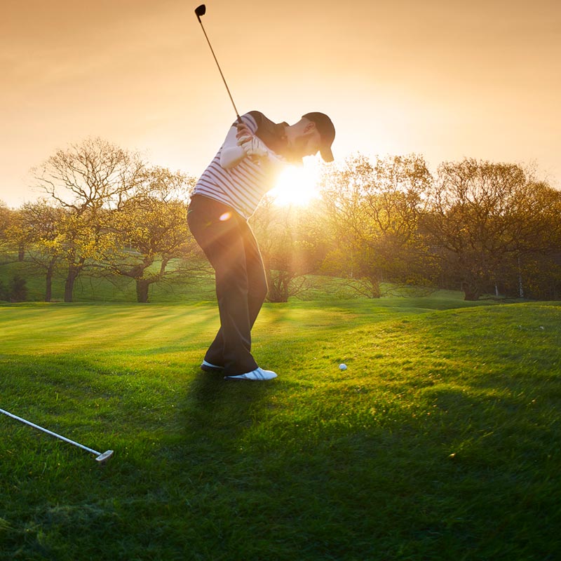 A man golfing with the sun in the background